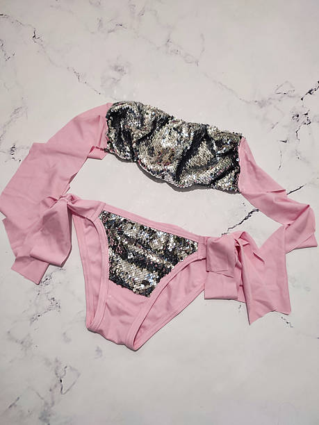 Pink bandeau bikini set with gray sequins flat lay close up at gray marble background. Two piece swimsuit, honeymoon women's summer beachwear, festive bikini with bows, cruise clothes, vacation