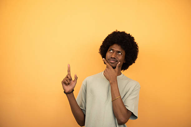 istock Young man pointing and thinking on orange background 2222272263
