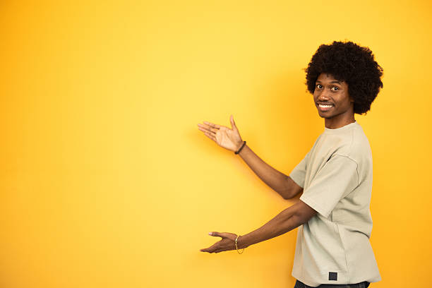 istock Young man showing something with hands on yellow background 2222272282
