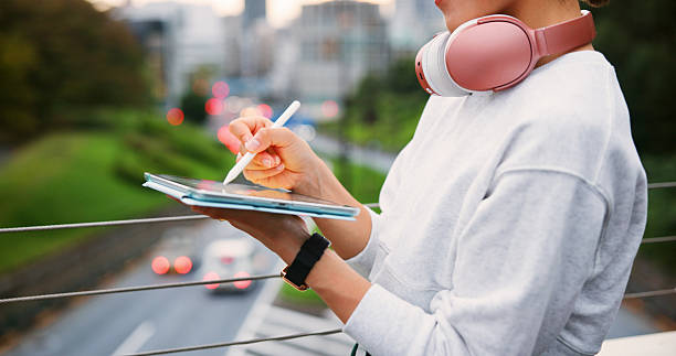 istock Hands, person and writing on tablet in city for copywriting, reading article and publishing process. Writer, headphones and pen of newsletter blog of story, editing update and project on bridge 2222272423