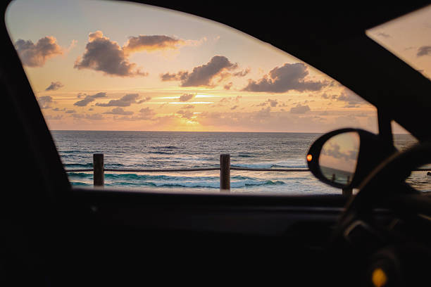 A dramatic sunset over the ocean, framed by the window of a parked car. View from inside vehicle with soft, golden light reflecting on the water.