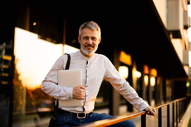 istock Smiling businessman holding laptop leaning on railing in urban setting 2222272908