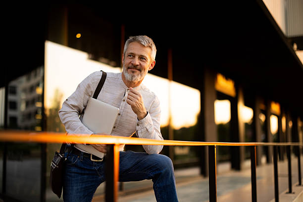 istock Smiling businessman leaning on railing outside office building at sunset 2222272924