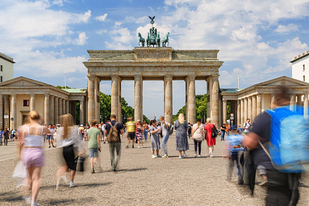 Tourists and pedestrians gathered at the historical Brandenburg Gate in Berlin under a sunny sky.