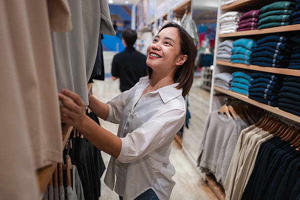 istock Young adult woman smiling while choosing clothes in a store, happily browsing through various garments on display racks 2222278437