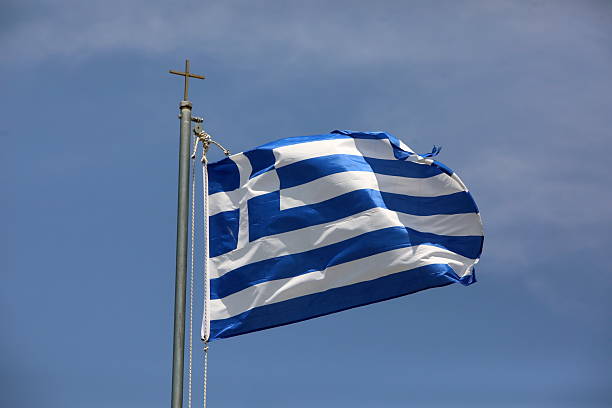 Behold the serene scene of the folded Greek flag, Orthodox flag, and a reverent cross