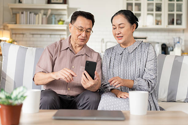 istock Asian senior couple enjoy using mobile phone on sofa. grandparent learning and connecting with social media, video call with family, shopping online, surfing the internet. 2222288004