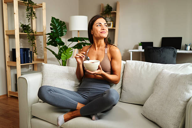 istock Young sportswoman eating healthy breakfast at home while sitting on sofa 2222289713