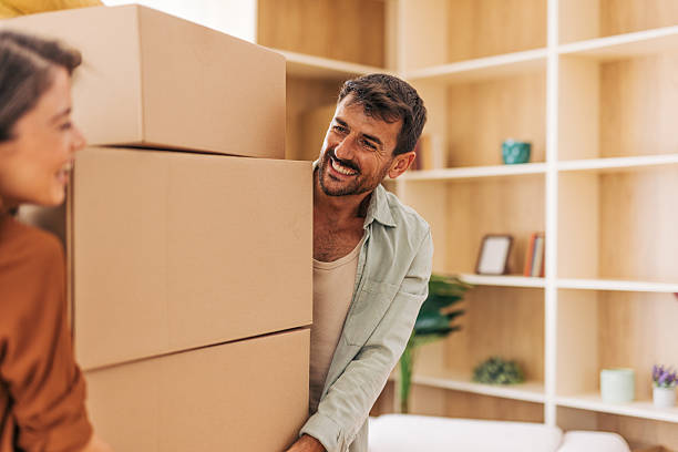 istock Happy couple carrying stacked cardboard boxes into new home 2222294101
