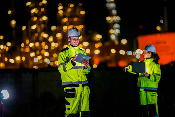 istock Female engineer in high visibility jacket uses a radio while analyzing data on a laptop during a night inspection at an industrial site, with blurred lights in the background. 2222294824