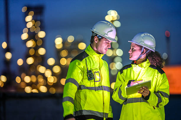 istock Two engineers in reflective safety gear review plans on a tablet during a night shift at an industrial site, with blurred factory lights glowing in the background. 2222295126