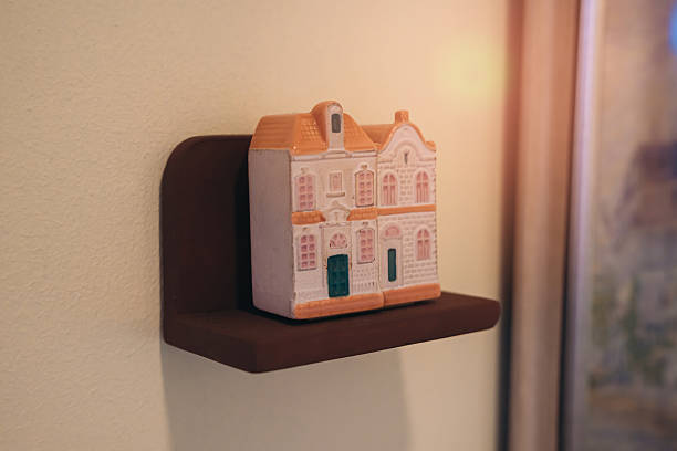 A charming decorative house figurine rests on a minimalist wall shelf, creating a cozy atmosphere with soft lighting. Perfect for home decor.