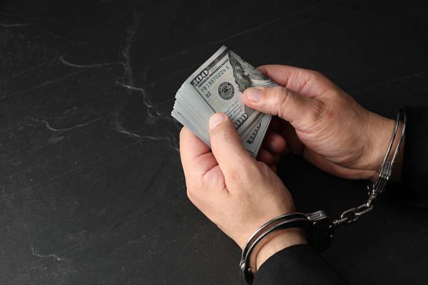istock Corruption. Man in handcuffs holding dollar banknotes at grey textured table, closeup 2222305954