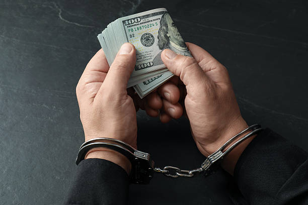istock Corruption. Man in handcuffs holding dollar banknotes at grey textured table, closeup 2222306024