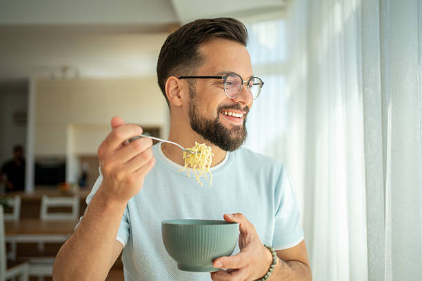 istock Happy man enjoying noodles while looking out the window 2222307791