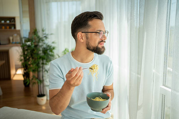istock Young man enjoying noodles while looking out the window 2222308698