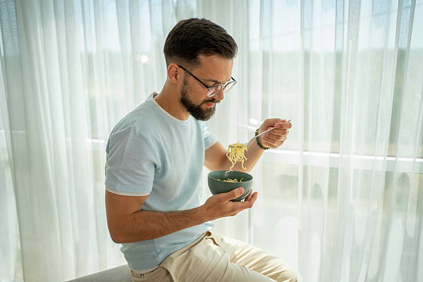 istock Young man eating noodles from bowl at home 2222308699