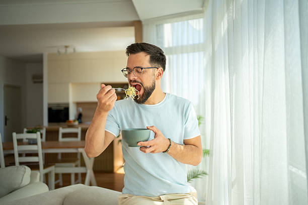 istock Young man enjoying noodles at home in natural light 2222308917