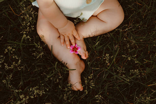 A close-up, high angle, cropped shot of a baby sitting in the grass, holding a flower. Shot with a Canon 5D Mark IV.