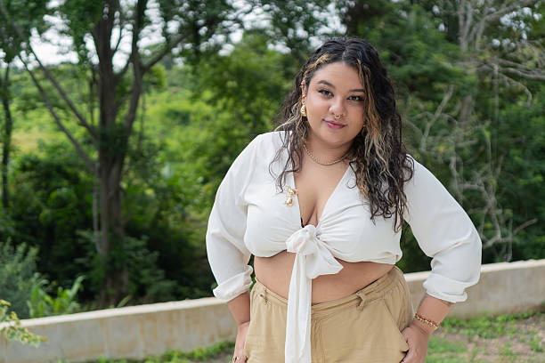 Plus-size, curvy fashion model posing outdoors, wearing a white top and beige pants