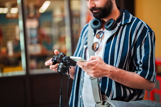 Engaged in documenting and sharing moments, a man seamlessly switches between his phone and camera amidst the backdrop of historic Turkish homes. The scene reflects modern connectivity and the blend of traditional architecture with digital storytelling.