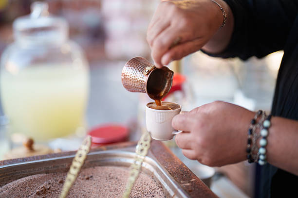 A close-up captures the pouring of Turkish coffee from pots roasted in hot sand, showcasing the traditional method and cultural richness of coffee preparation. The scene evokes the aroma and ritual of Turkish coffee tradition.