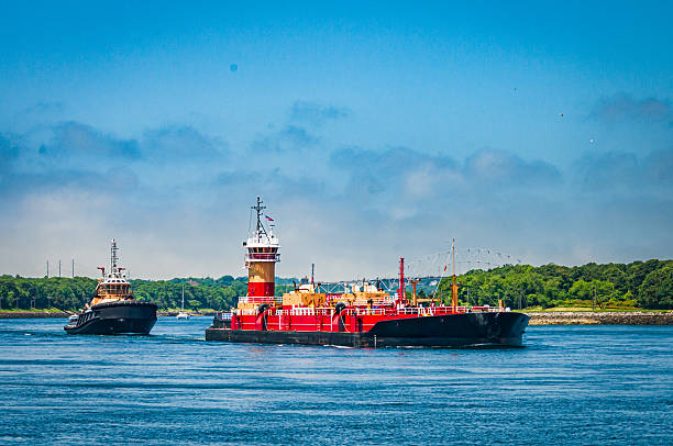 A pair of tug boats push a barge through the Cape Cod canal.  One acts as a pusher, while the second tug watches to make sure the barge stays on its designated course.