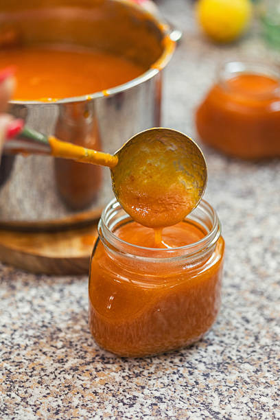A woman prepares and canned fresh homemade apricot jam. She pouring him into a jar