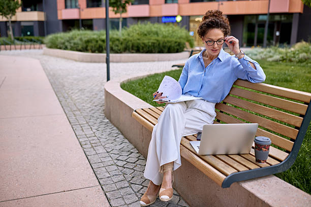 istock Businesswoman working on laptop and reviewing documents while sitting on bench 2222331815