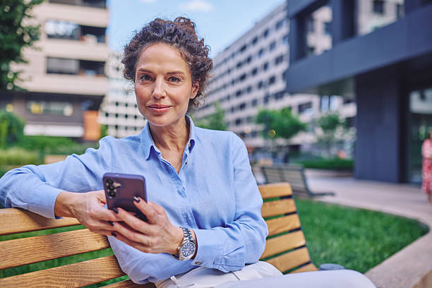 istock Businesswoman using smartphone and smiling while sitting on bench in city park 2222331861