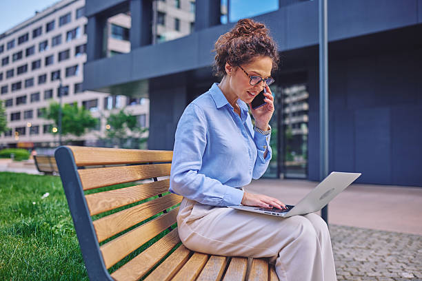 istock Businesswoman working with laptop and talking on phone while sitting on bench 2222331863