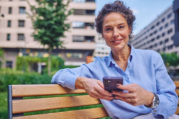 istock Businesswoman smiling and using smartphone while sitting on bench 2222331879