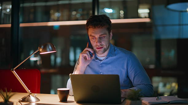 istock Multitasking ceo talking cellphone looking laptop screen at night office closeup 2222332502
