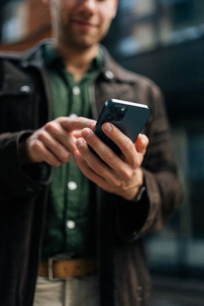 istock Vertical selective focus shot of unrecognizable man holding and using smartphone standing on city street, browsing internet, checking social media 2222337533