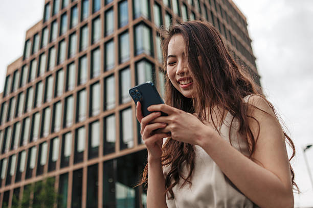 istock Young Asian Woman Using Smartphone in front of Modern Office Building 2222338290