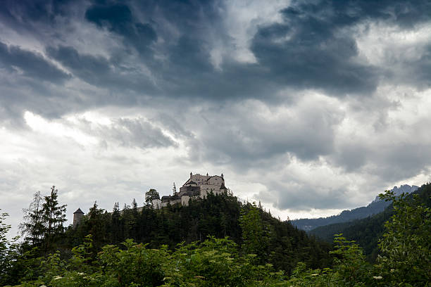 Werfen, Austria - 21 June 2019: Dramatic landscape before thunderstorm with medieval rock Hohenwerfen castle on forested mountain. Stormy scenery with old palace by dark clouds sky in Salzburger land, Austria