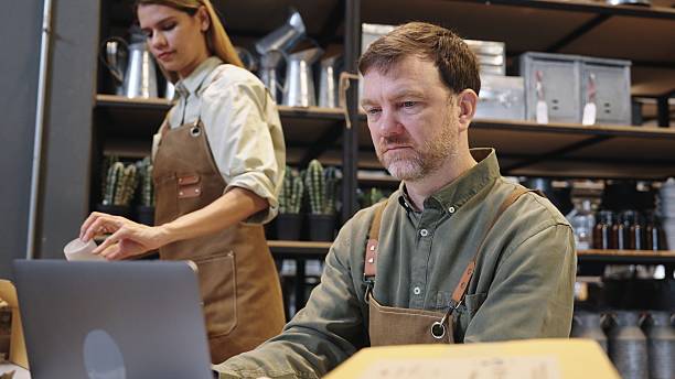 istock Two small business warehouse worker wearing green apron checking reviewing inventory working with  computer while examining products with gardening and art craft Sustainability friendly zero waster and plastic free  quality control in a hands-on business 2222351079
