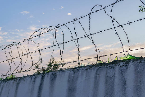 istock Barbed wire and broken glass protecting concrete wall at sunset 2222359582