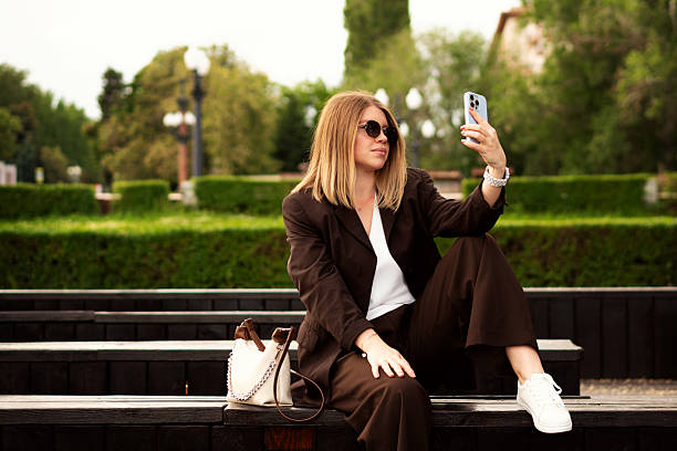 Young woman sitting outdoors on bench taking selfie with smartphone
