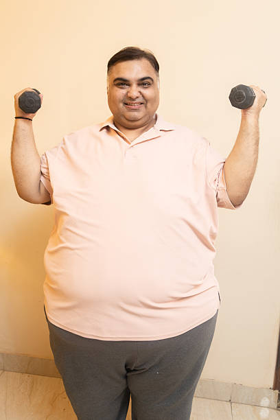istock Overweight fat indian man using dumbbells for sports exercise. Plus size chubby male try to lose weight. Obesity problem. Fitness Challenge and motivation. 2222360426
