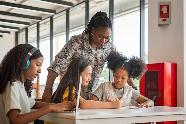 istock Teacher Guiding Diverse Students in a Modern Classroom, Educator Assisting Children with Schoolwork and Laptops, Multi-ethnic Group of Kids Learning Together with an Instructor 2222364822