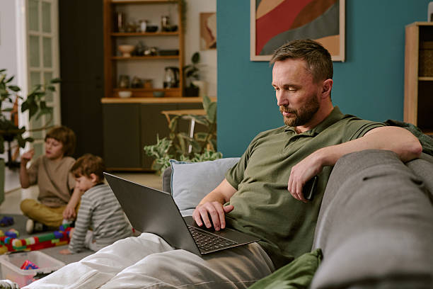 istock Middle Aged Man Working Remotely on Laptop While Children Playing 2222369199