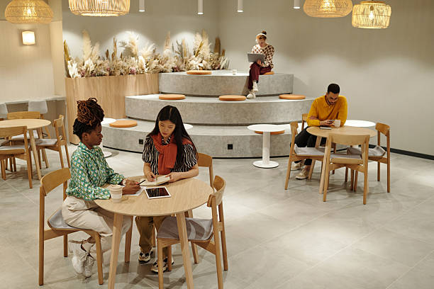 Black and Asian women collaborating at round table in modern coworking space, young adult men working in background
