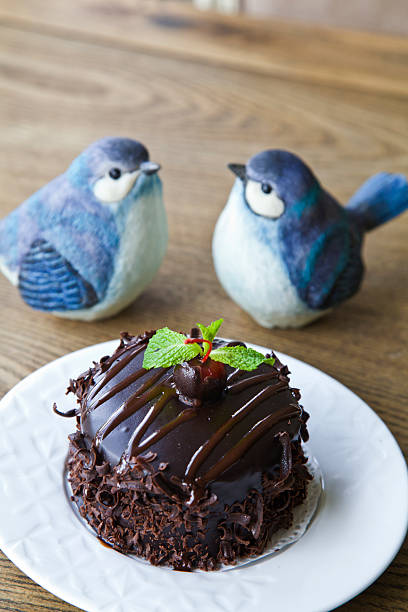 Close-up of two rich chocolate balls decorated with white icing and colorful sprinkles, placed in paper cups on a rustic wooden table. Ideal for dessert concepts.
