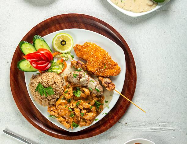 Premium western meal with various chicken dishes: schnitzel, sliced breast, cordon bleu, and shish tawook, top view, white background.