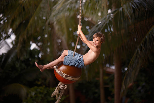 Carefree boy having fun on a rope swing in summer day.