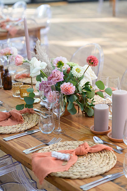 A beautifully styled rustic table setting adorned with a lovely floral centerpiece. The decor features soft pastel tones combined with natural wicker details, creating an elegant and intimate atmosphere. Each place setting is meticulously arranged with care, perfect for celebrations or weddings. The addition of candles and woven placemats enhances the charm.