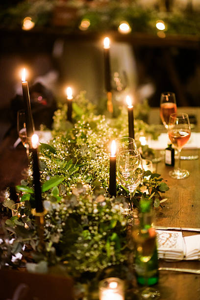 A beautifully decorated reception table highlighted with lush greenery, soft candlelight, and sparkling glassware. The ambiance exudes an intimate, elegant atmosphere perfect for celebratory gatherings or weddings. Black candles add sophistication, complementing the natural and rustic theme. A flawless blend of warmth and style.