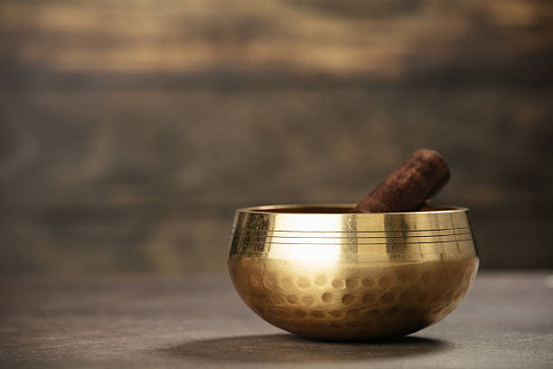 A polished golden singing bowl with a wooden mallet, perfect for meditation and sound therapy, placed on a rustic wooden surface.