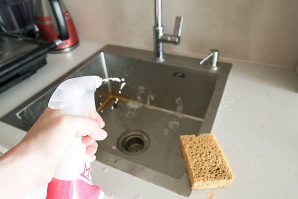 Step-by-step cleaning of a stainless steel kitchen sink using a sponge and cleaning spray to remove food residue and stains.